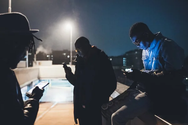 Tres amigos africanos sentados al aire libre y mirando el teléfono inteligente — Foto de Stock