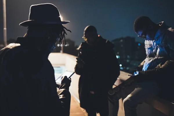 Τρεις Αφρικανοί φίλοι κάθονται σε εξωτερικούς χώρους και αναζητούν το smartphone — Φωτογραφία Αρχείου