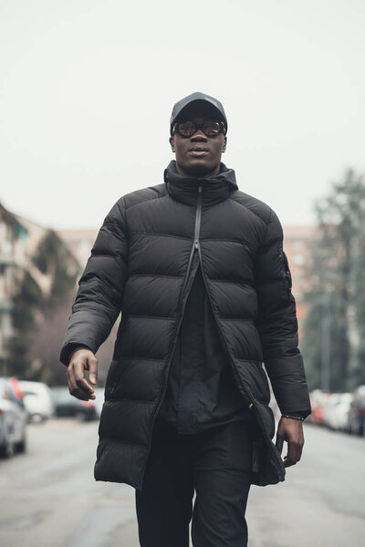 Молодой бородатый африканский мужчина на улице ходит, глядя в камеру
 