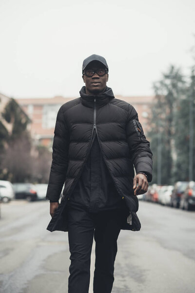 Молодой бородатый африканский мужчина на улице ходит, глядя в камеру
 