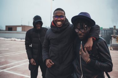 Üç genç Afrikalı adam birlikte sarılıp eğleniyorlar.