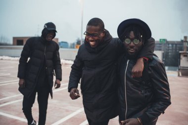 Üç genç Afrikalı adam birlikte sarılıp eğleniyorlar.