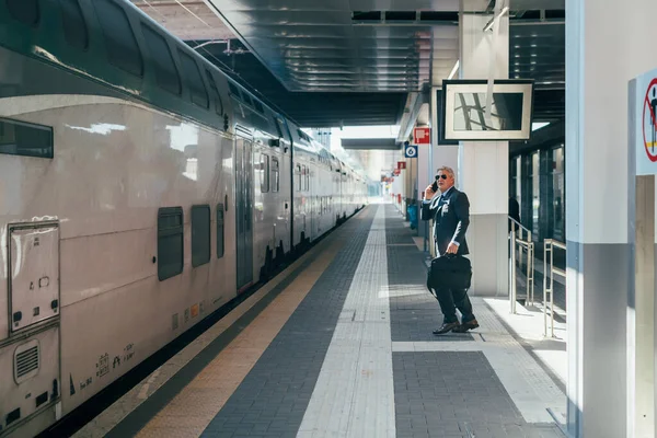 スマートフォンを話す鉄道駅の中世のビジネスマン 会話携帯電話を持つ電車に乗るビジネスマン — ストック写真