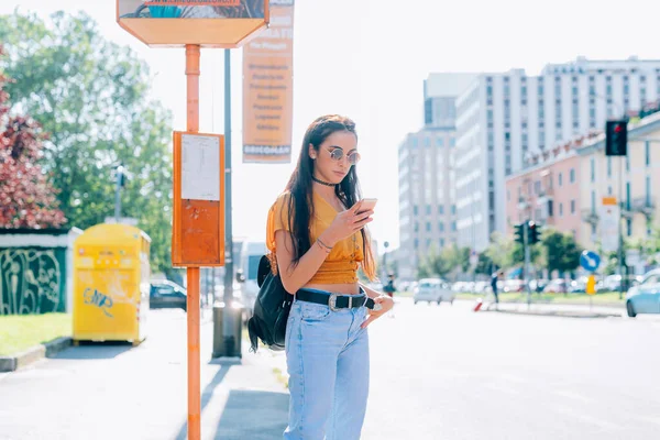 Młoda Kobieta Czeka Zewnątrz Przystanku Autobusowym Pomocą Smartfona Technologia Podróżnik — Zdjęcie stockowe