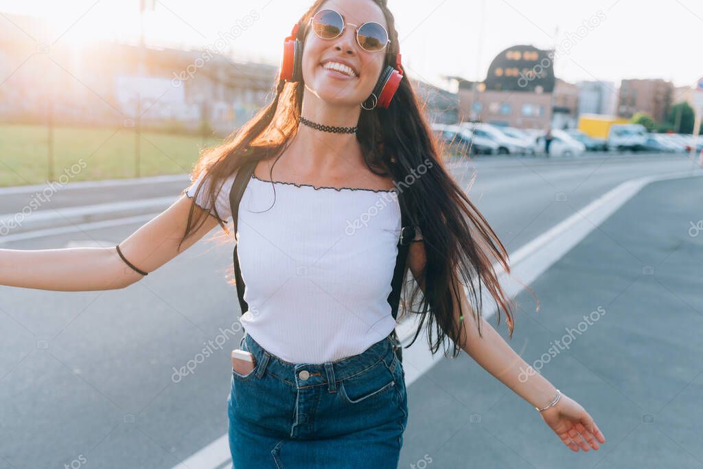 young woman outdoor listening music laughing and dancing back light - happiness, toothy smile, music concept