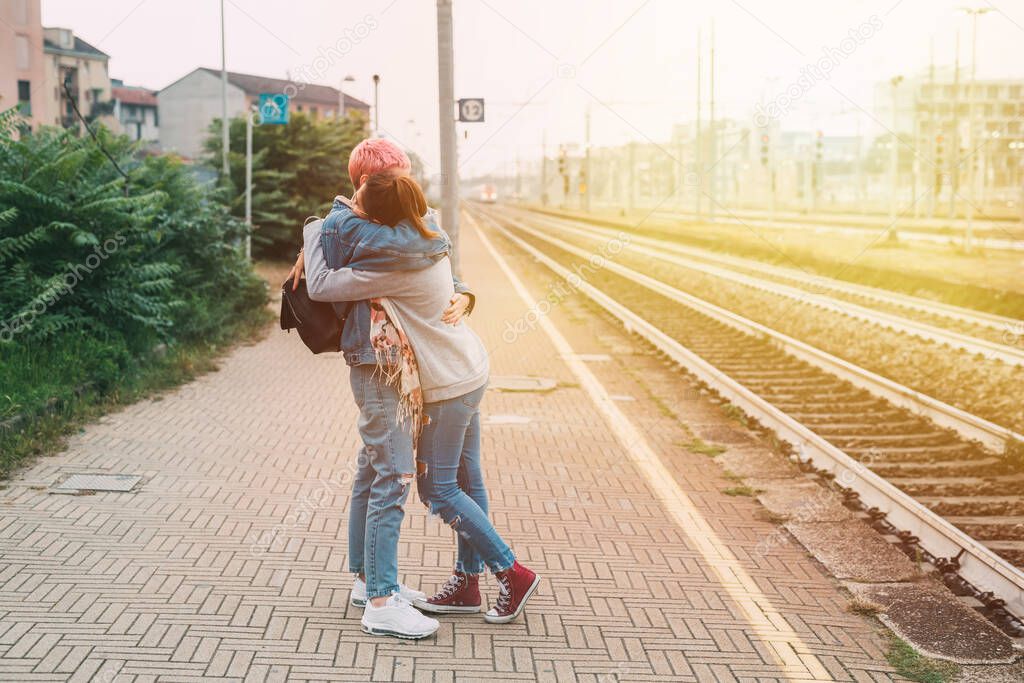 Female friends hugging railway platform saying goodbye - Two young millennials women affectionate meeting hugging train station