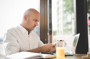 Yetişkin adam evde dizüstü bilgisayar ve akıllı telefon kullanarak çalışıyor.