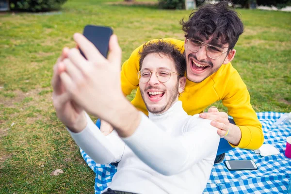 İki erkek arkadaş dışarıda Selie 'yi eğlendiriyorlar - erkek arkadaşlar akıllı telefon kullanarak gülüyorlar - teknoloji, mutluluk, sosyal konsept
