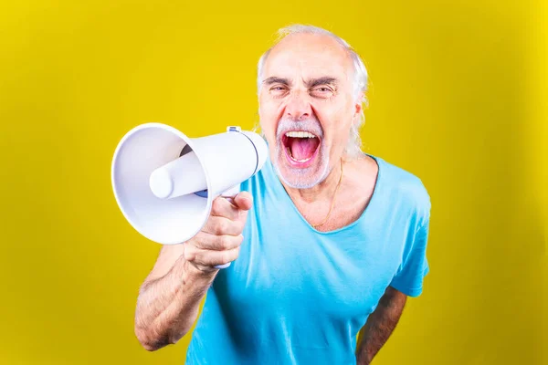 Senior man screaming loudly in a megaphone on yellow background -Elderly beautiful grey-haired man demonstrating using megaphone over isolated yellow background - defending, activist, protest concep