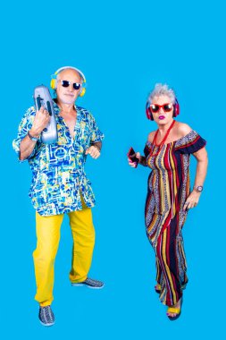 Mavi arka planda bir çift son sınıf erkek ve kadın müzik seti ve akıllı telefondan soyutlanmış dedem ve ninem dans ediyor teknoloji, gece kulübü, eğlenceli konsept.