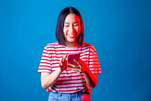 若い美しいアジアの女性が青い背景にスマートフォンをテキストメッセージ スマートフォンの笑顔のスタジオショットを使用して隔離されたアジアの若い女性 ソーシャルネットワーク 多様性の概念 — ストック写真