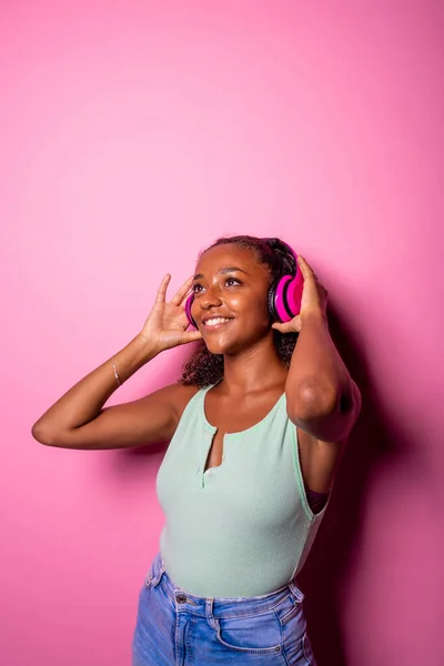 ピンクの背景で陽気な黒人女性が音楽を聴く 黒の若い女の子はヘッドフォンを身に着けて踊る笑顔 自信を持って 音楽の概念 — ストック写真