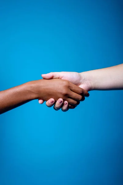 Black and white women hands handshake showing each other friendship and respect on blue background - Isolated diverse multiethnic female hands supporting - brotherhood, racism, equality concept