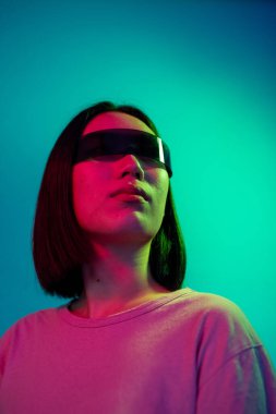 Renkli arka planda akıllı gözlük takan Asyalı genç bir kadın - arka planda izole edilmiş bilim kurgu gözlükleri takan farklı genç bir kadın - artırılmış gerçeklik, uygulanabilir teknoloji, bilim kurgu konsepti