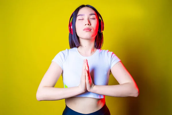 Asiatic young woman listening music meditating on yellow background - Female asiatic isolated relaxing doing yoga listening music -  harmony, calming, spirituality concept