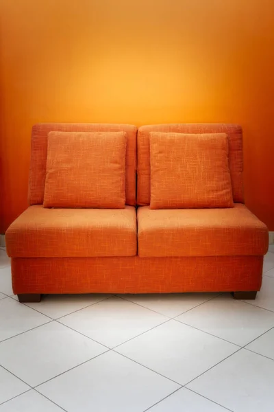 橙色沙发 有两个座位和两个枕头在橙色的墙壁和白色的地板 — 图库照片