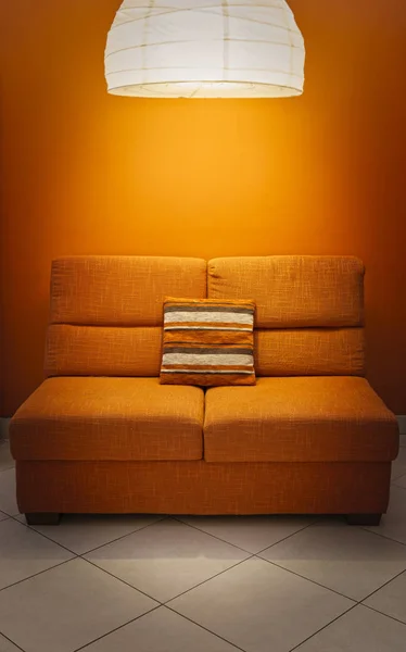 Orange sofa and wall with lamp above and pillow