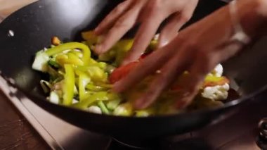 Kadın şef biber, kabak, karnabahar ve domatesleri büyük siyah metal bir tavada hazırlar ve karıştırır.