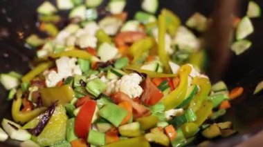 Şef karnabahar, biber, domates ve kabakları büyük metal bir tavada ahşap bir kaşıkla karıştırır.