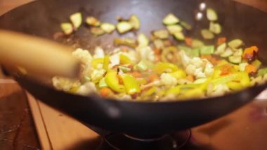 Şef karnabahar, biber, domates ve kabakları büyük metal bir tavada ahşap bir kaşıkla karıştırır.