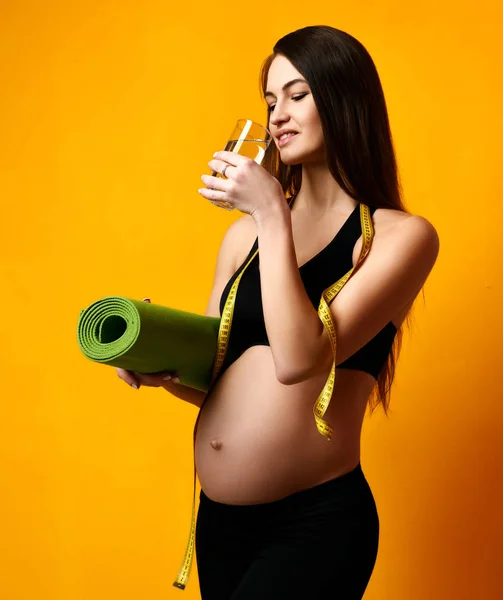 Concept de grossesse. Femme enceinte boire de l'eau tenir sport tapis de yoga vert pour l'entraînement et le ruban à mesurer — Photo