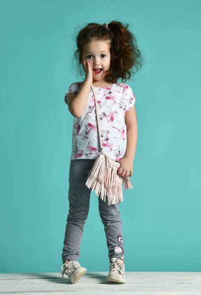 Cute curly baby girl kid in white t-shirt and blue jeans smiling on blue mint — Stock Photo, Image