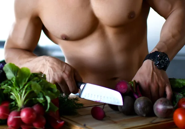 Мускулистый спортсмен, стоящий на кухне с овощами в руках держат редис, глядя в угол улыбаясь — стоковое фото