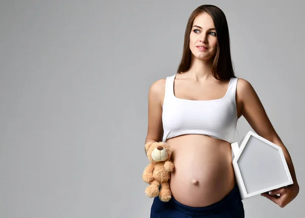 Embarazada mujer en blanco top camisa hold casa y osito de peluche —  Fotos de Stock