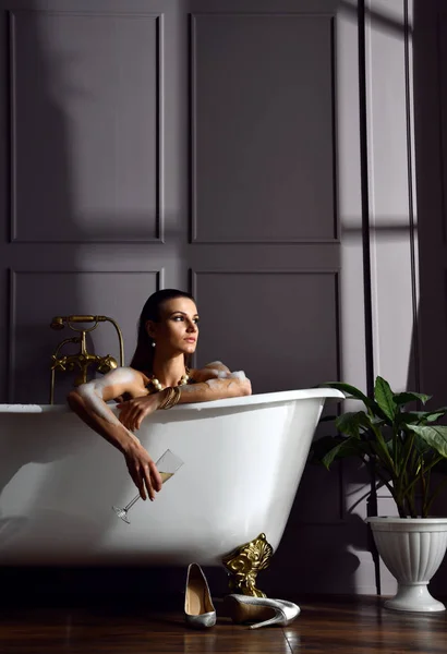 Ung vacker kvinna som sitter i badrum nära dyra badkar badkar titta i hörnet på mörk — Stockfoto