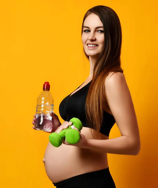 Femme enceinte entraînement prêt avec de petits haltères poids sur fond jaune tenir bouteille d'eau — Photo