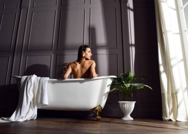 Banyoda karanlık köşede bakarak pahalı küvet banyo yakın oturan genç güzel kadın 