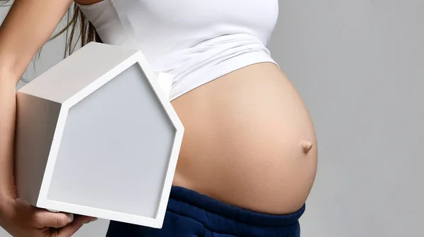 Gravid kvinna i vit topp skjorta hålla lilla vita huset och nycklar på grå — Stockfoto