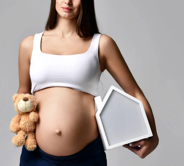 Embarazada mujer en blanco top camisa hold casa y osito de peluche —  Fotos de Stock