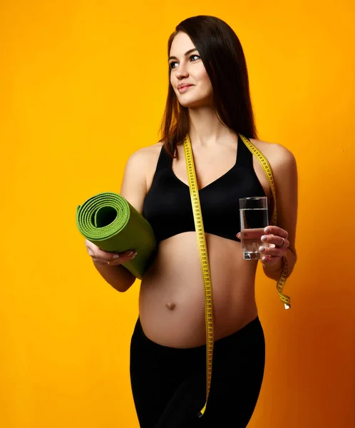 Schwangerschaftskonzept. schwangere Frau trinkt Wasser halten Sport grüne Yogamatte für Workout und Maßband — Stockfoto