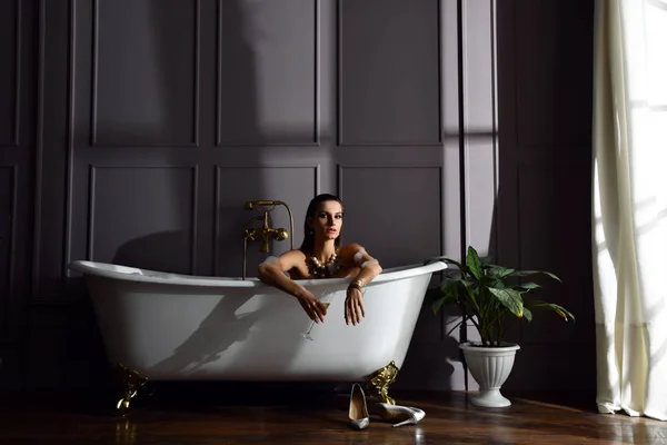 Joven hermosa mujer sentada en el baño cerca de bañera cara bañera mirando a la esquina en la oscuridad —  Fotos de Stock