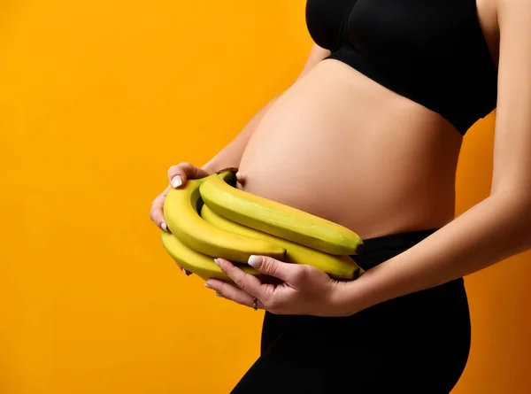 Concetto di gravidanza. Donna incinta tenere banana vicino all'addome sul giallo — Foto Stock