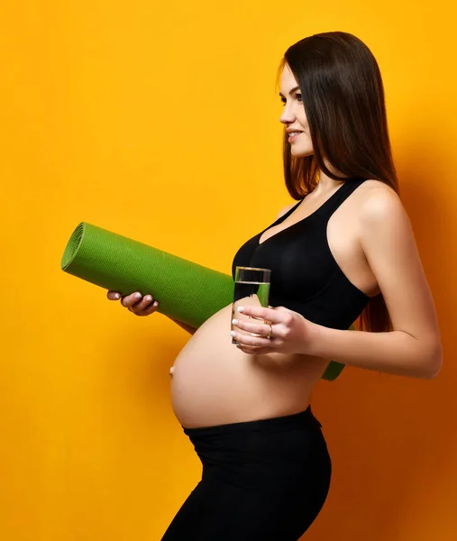 Concepto de embarazo. Embarazada mujer beber agua hold deporte verde yoga mat para entrenamiento y cinta métrica —  Fotos de Stock