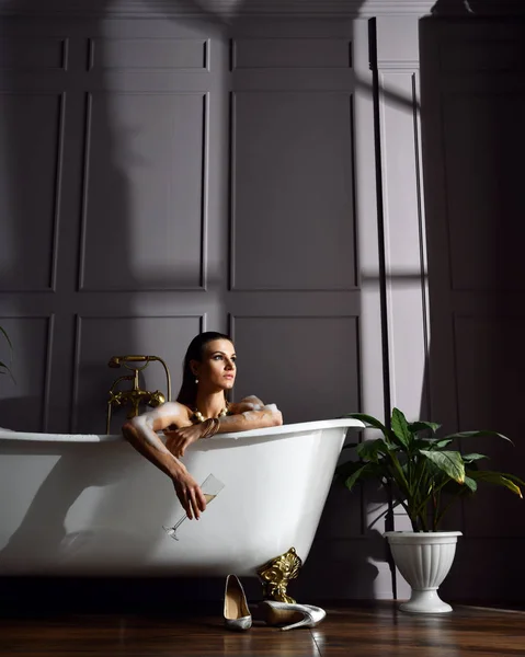 Young beautiful woman sitting in bathroom near expensive bathtub bath looking at the corner on dark — Stock Photo, Image