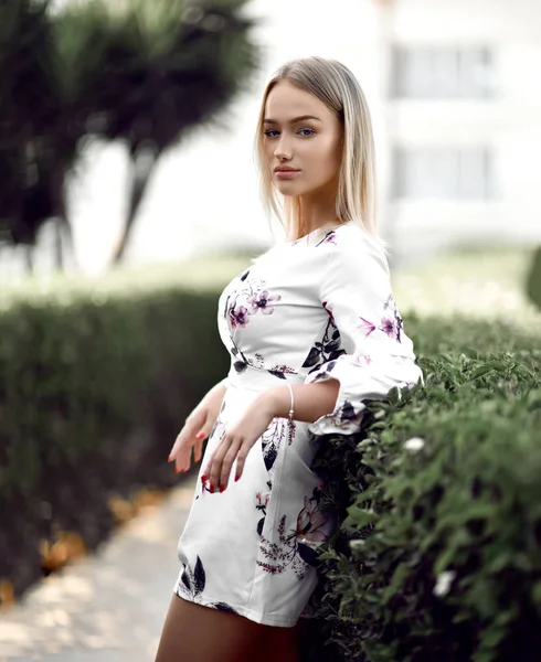 Joven chica rubia hermosa posando en el complejo forestal tropical en vestido blanco casual con flores — Foto de Stock