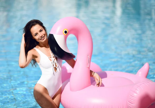 年轻性感漂亮的女人在游泳池休闲放松与巨型充气巨型粉红色火烈鸟浮动床垫白色比基尼 — 图库照片