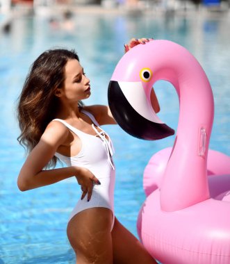 Genç seksi kadın rahatlatıcı bir yüzme havuzu boş zaman içinde dev şişme dev pembe flamingo float yatak beyaz bikini ile güzel