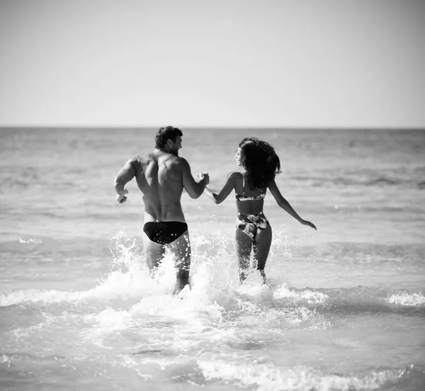 Feliz pareja alegre divirtiéndose abrazándose corriendo en el mar juntos. Vacaciones románticas, amor de luna de miel —  Fotos de Stock