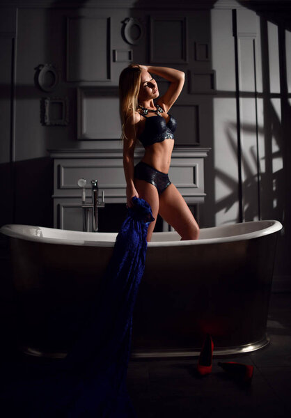 Young beautiful woman sitting in bathroom near expensive bathtub bath looking at the corner on dark 