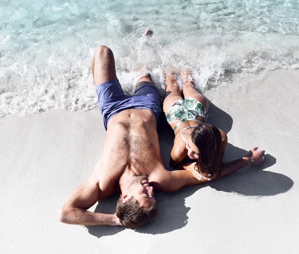Ευτυχισμένο ζευγάρι χαρούμενα διασκεδάζοντας ξαπλωμένος στην άμμο της παραλίας στη θάλασσα ακτή μαζί. Ρομαντικές διακοπές, μήνα του μέλιτος αγάπη — Φωτογραφία Αρχείου