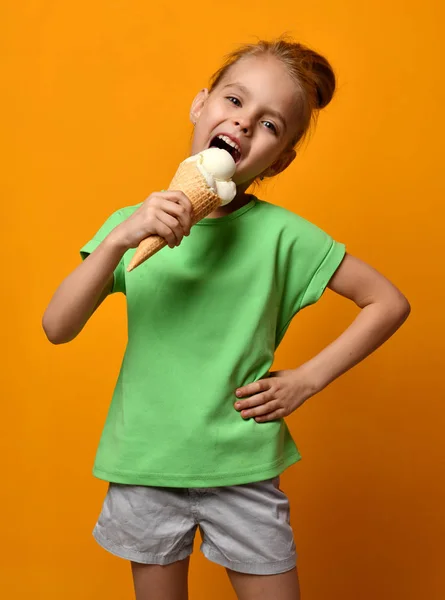 Pretty bebé niña comer lamiendo helado de vainilla en gofres cono sobre fondo amarillo —  Fotos de Stock