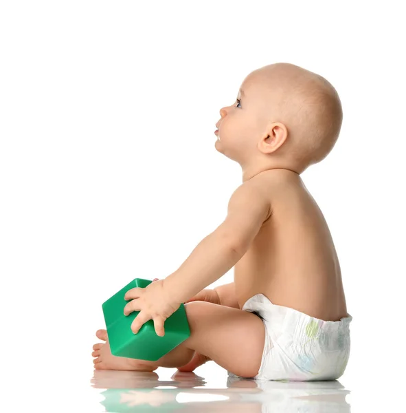 Малыш сидит голый в подгузнике с зеленой кирпичной игрушкой и смотрит вверх — стоковое фото