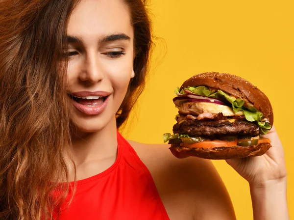 Mujer de cerca mira el gran sándwich de hamburguesa barbacoa con boca hambrienta feliz sonriendo sobre fondo amarillo — Foto de Stock