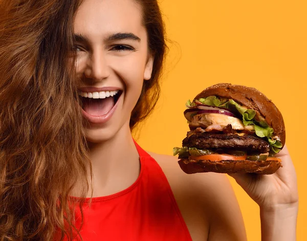 Mujer sostener gran bocadillo de hamburguesa de res con huevo con boca hambrienta feliz riendo sobre fondo amarillo — Foto de Stock