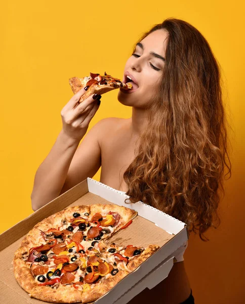Молодая красивая женщина есть пиццу пепперони ломтик и держать целую пиццу в коробке — стоковое фото