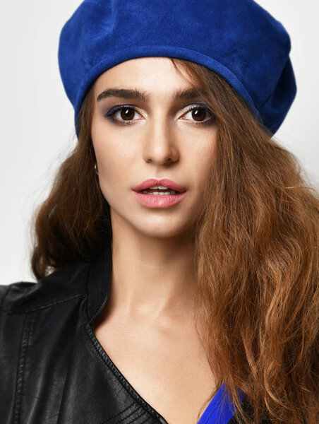 brunette woman in blue beret hat looking at the camera on gray background